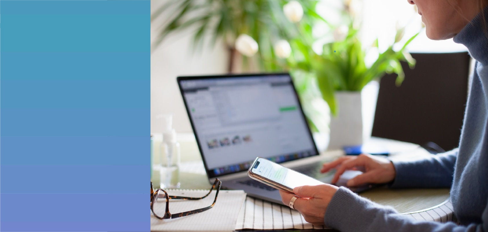 Person using a mobile phone while typing on a laptop.